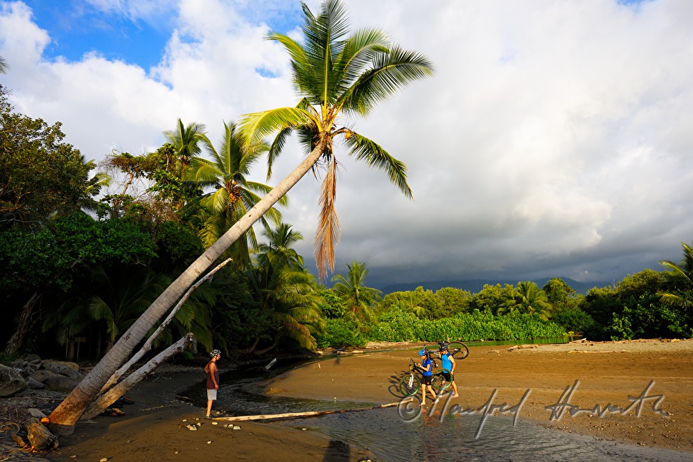 mountainbikers cross a river at the ocean