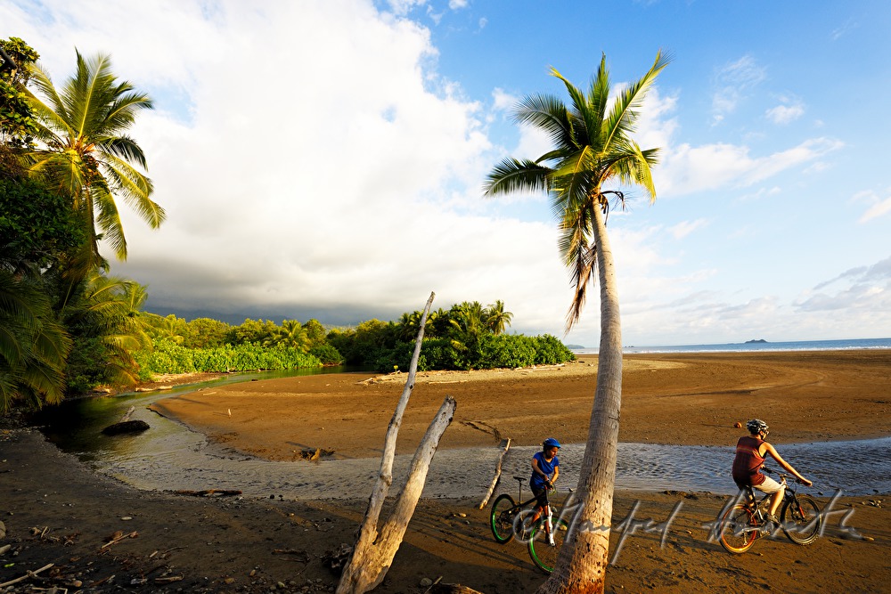 mountainbikers cross a river at the ocean